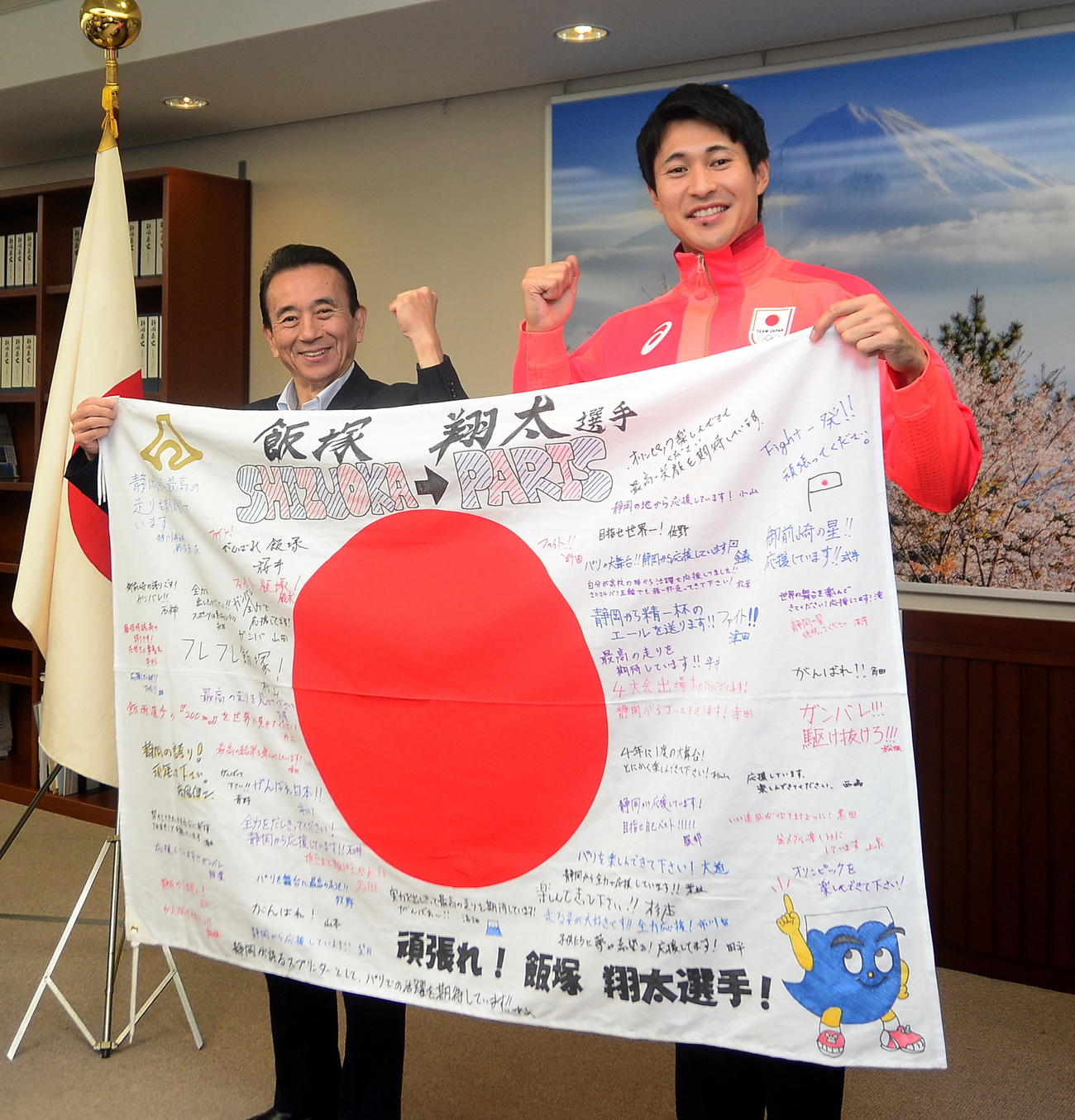 応援メッセージが書かれた国旗を手に記念撮影に収まるパリ五輪・陸上男子200メートル代表の飯塚（右）