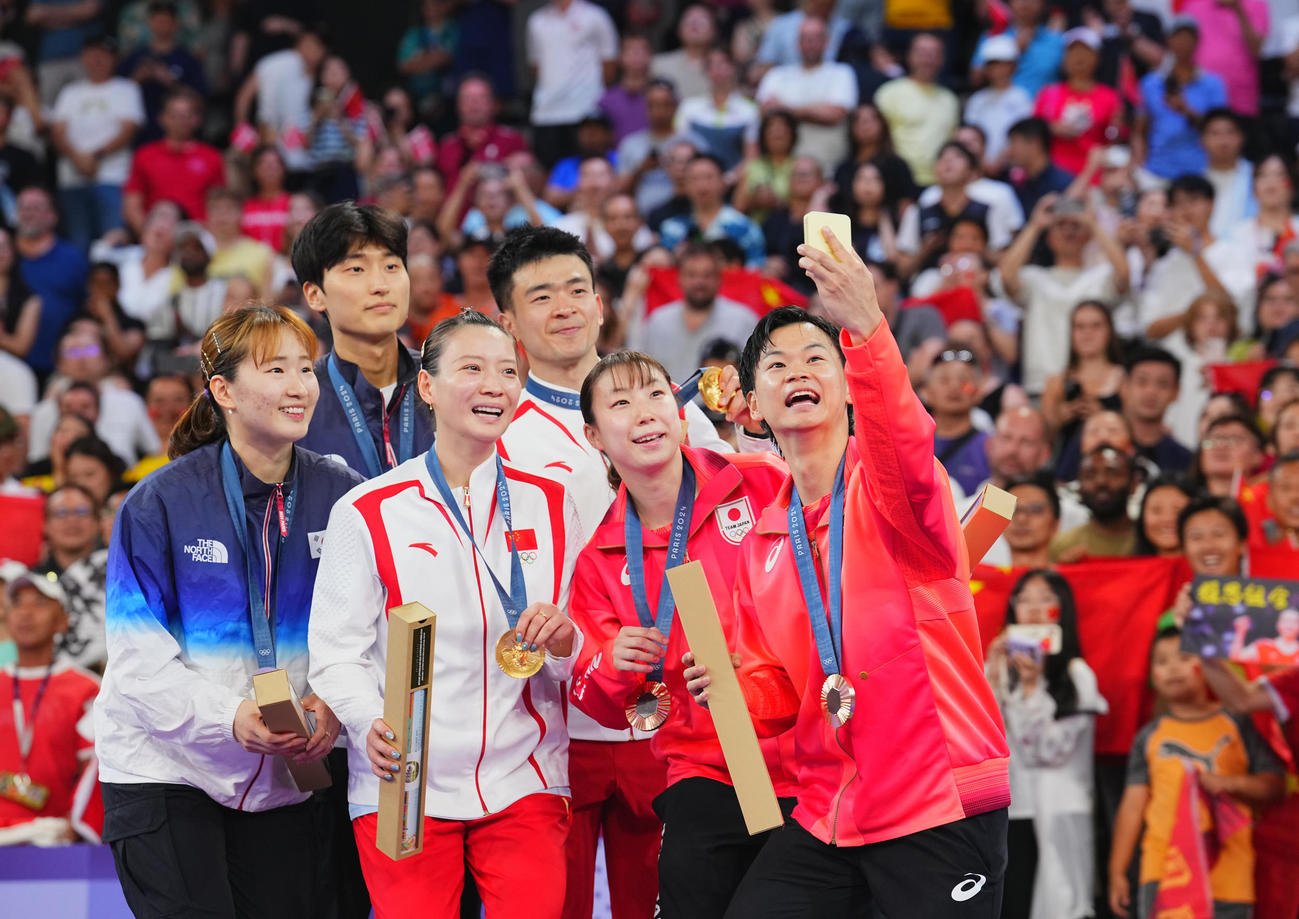 バドミントン混合ダブルス3位決定戦、表彰台でセルフィーの撮影を務める渡辺（右）。同2人目は東野組（撮影・垰建太）