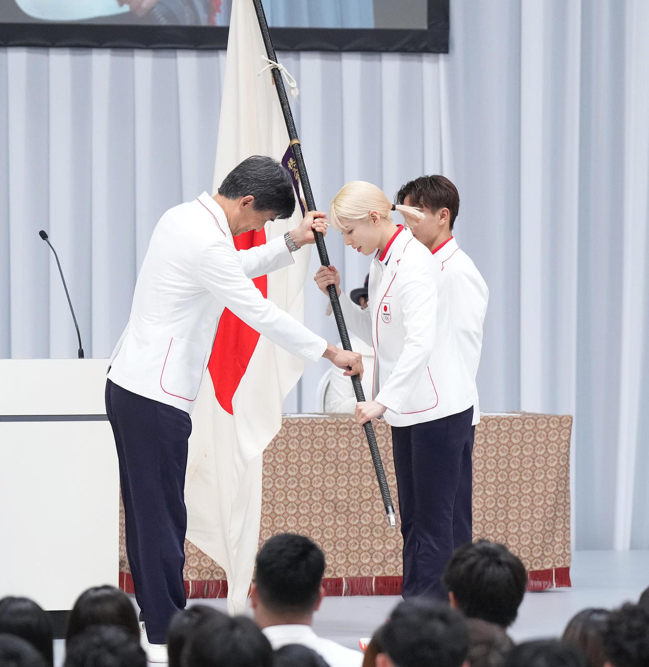TEAM JAPAN結団式で団長の尾県（左）から団旗を受け取る旗手の江村（中央）と半井（撮影・菅敏）