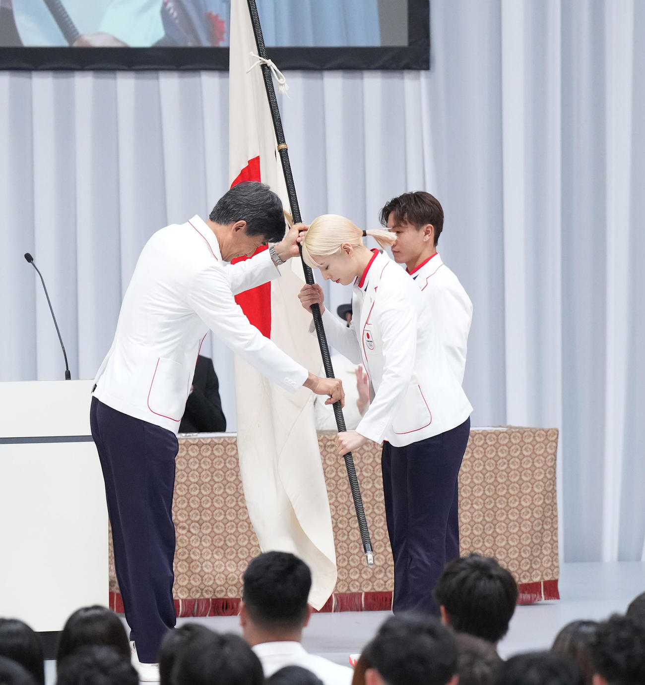 TEAM JAPAN結団式で団長の尾県（左）から団旗を受け取る旗手の江村（中央）と半井（撮影・菅敏）