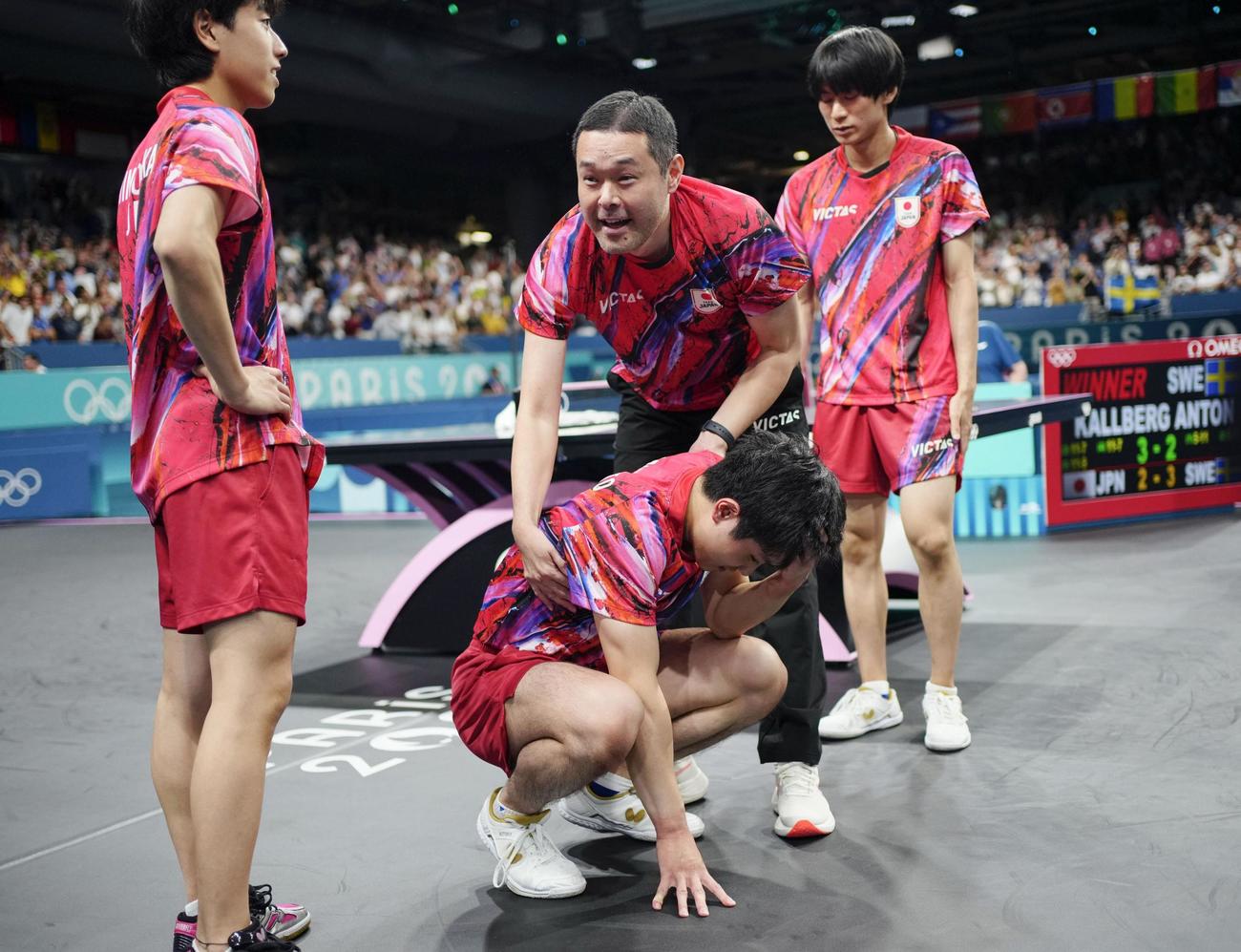 男子団体準決勝でスウェーデンに敗れ座り込む張本智和をねぎらう田勢邦史監督。左は篠塚大登、右は戸上隼輔（共同)