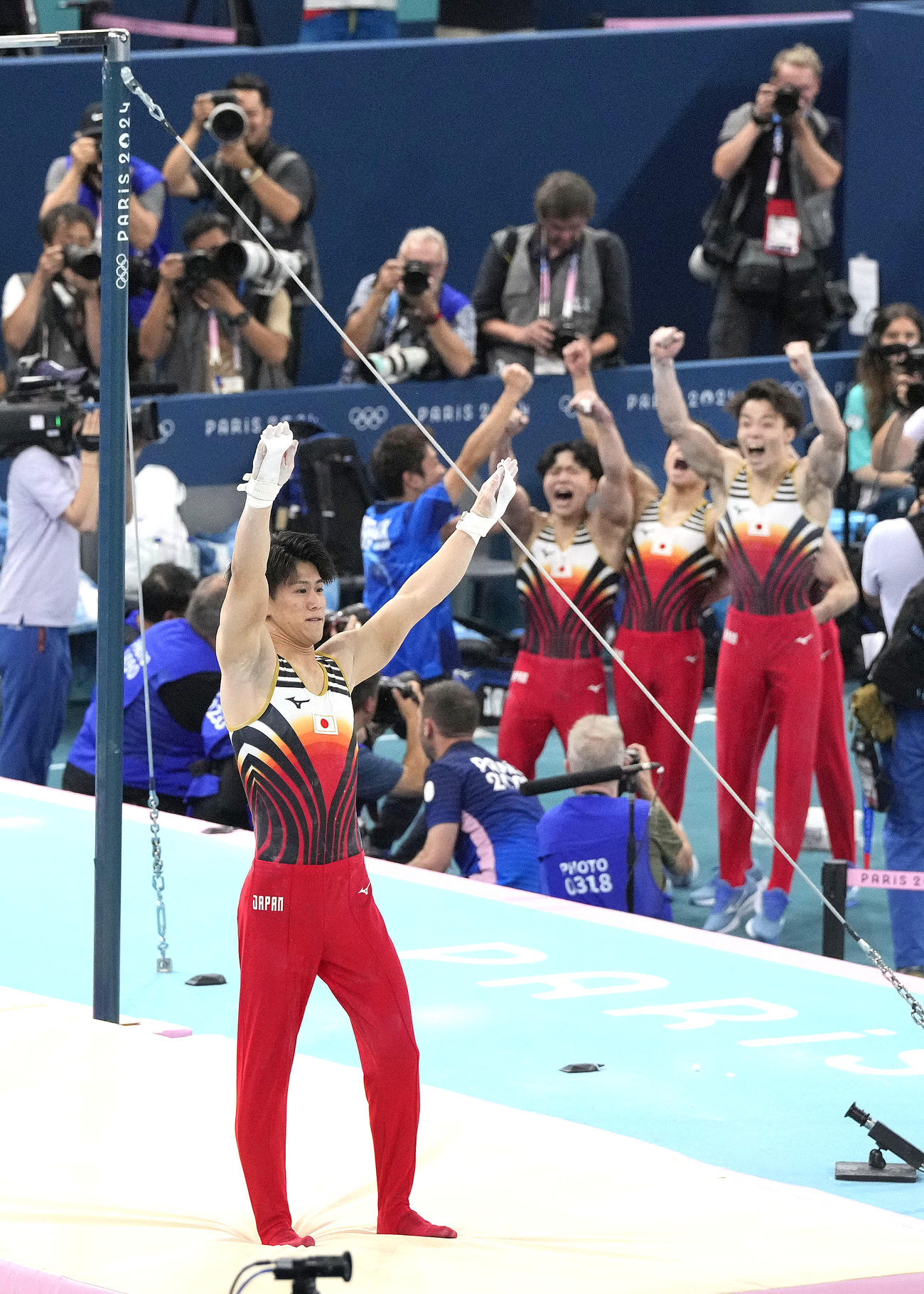 男子団体総合決勝　最終種目の鉄棒で着地を決めた橋本大輝と喜ぶ日本チーム（共同）