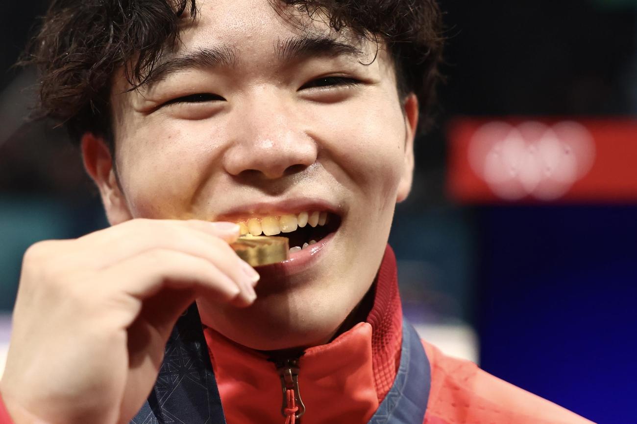男子個人総合で優勝し、金メダルを笑顔でかじる岡（撮影・河田真司）