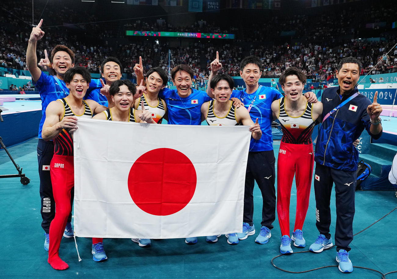 体操男子団体決勝、金メダルを決め日の丸を手に写真に納まる日本の選手、関係者たち（撮影・垰建太）