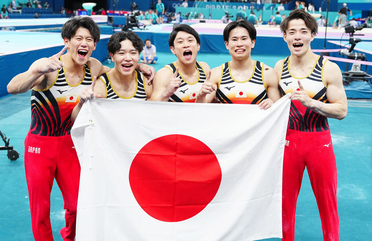 体操男子団体決勝、金メダルを決め日の丸を手に写真に納まる日本の選手たち。左から橋本、岡、谷川、萱、杉野（撮影・垰建太）