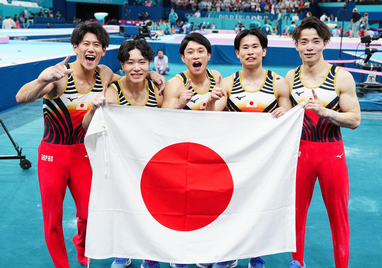 体操男子団体決勝、金メダルを決め日の丸を手に写真に納まる日本の選手たち。左から橋本、岡、谷川、萱、杉野（撮影・垰建太）