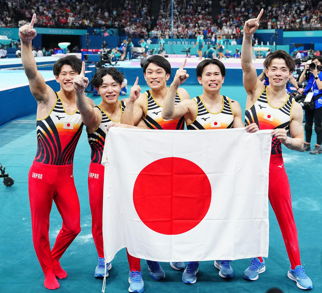体操男子団体決勝、金メダルを決め日の丸を手に写真に納まる日本の選手たち。左から橋本、岡、谷川、萱、杉野（撮影・垰建太）