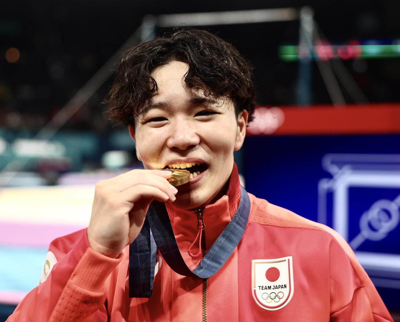 男子個人総合で優勝し、金メダルを笑顔でかじる岡（撮影・河田真司）