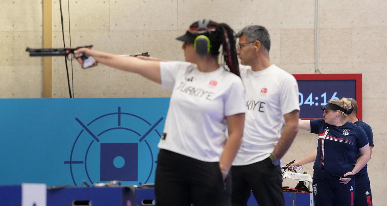 パリ五輪の射撃混合エアピストルにTシャツ無装備で出場し、左手をポケットに入れながら銃を撃つトルコのユスフ・ディケチュ（右）。左はセブヴァル・イライダ・タルハン（ロイター）