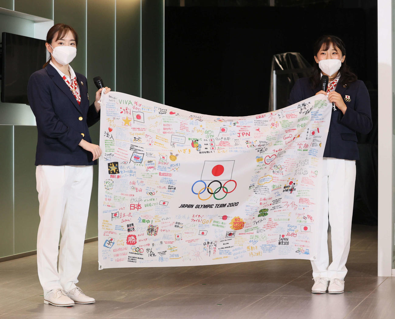 日本代表選手団壮行会で、応援メッセージが書かれた旗を広げる副主将の石川（左）と旗手の須崎（代表撮影）