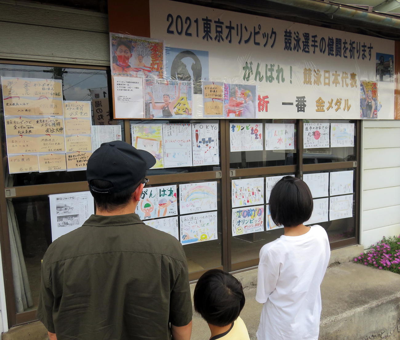 東御市指定文化財「一番観音」脇の競泳日本代表応援コーナーを見つめる家族（撮影・鎌田直秀）
