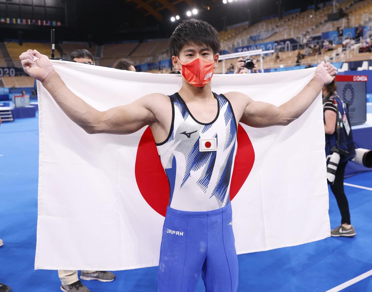 男子種目別鉄棒決勝で金メダルを獲得し、日の丸を背にする橋本大輝（共同）