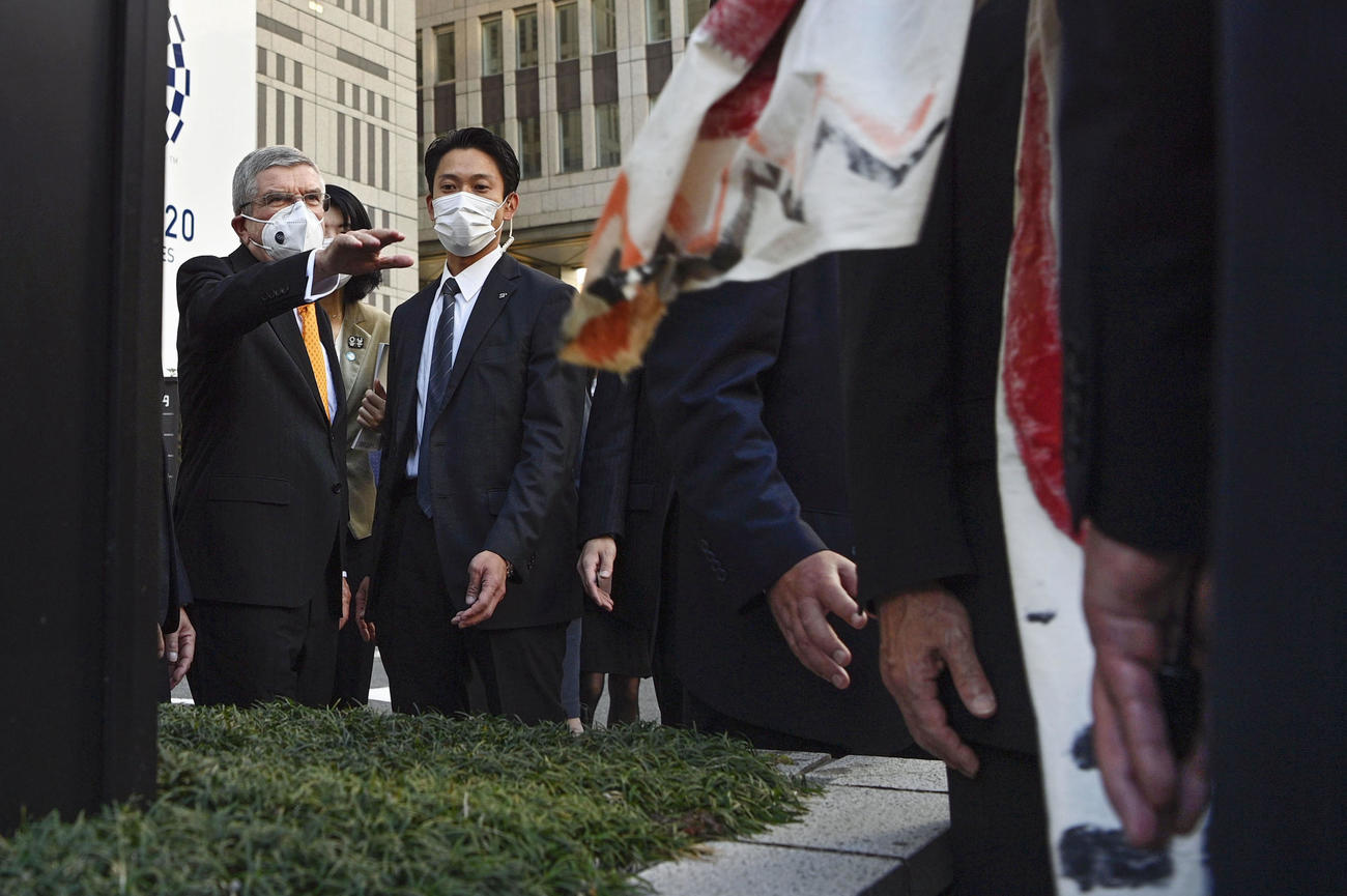 東京都知事と会談後、横断幕を手に待ち受けていた五輪反対派の市民と言葉を交わすIOCのバッハ会長（左端）（共同）