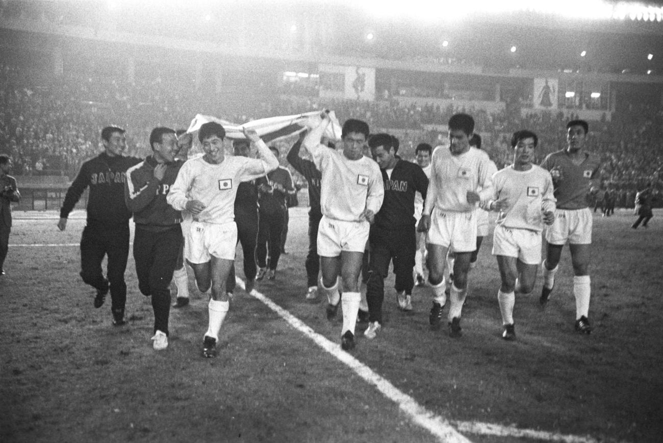 ッカーアジア第1組予選　日本1－0南ベトナム　南ベトナムに勝ち、得失点差で韓国を上回り五輪代表切符を手にした日本イレブン、日の丸を掲げ場内を1周。白ユニホーム左から山口芳忠、杉山隆一、森孝慈、片山洋、横山謙三（1967年10月10日撮影）