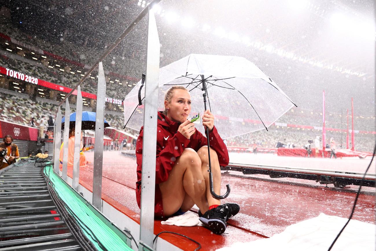 突然の大雨に傘を差して身を小さくする陸上女子棒高跳びのマラーチョバ（チェコ）（ロイター）