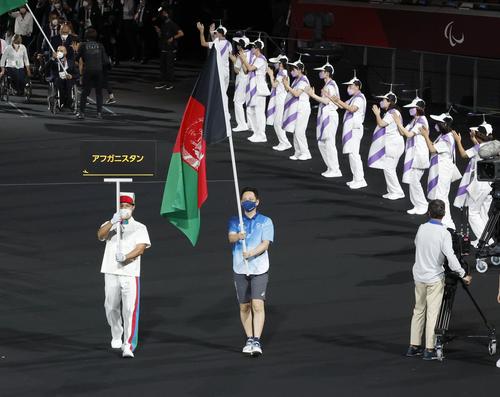 政治情勢の緊迫化で参加できなかった代表団に代わって、アフガニスタンの国旗を掲げて入場するボランティア=24日夜、国立競技場(共同)