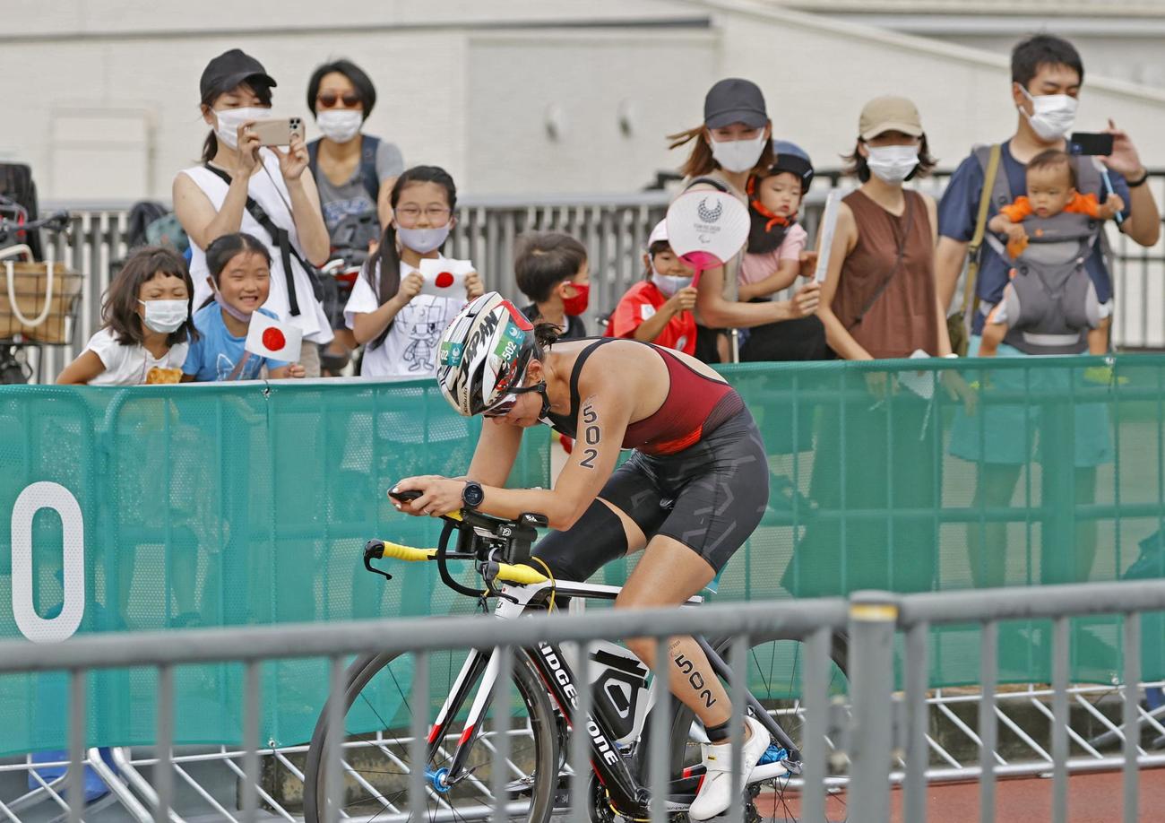 女子（運動機能障害PTS5）　バイクで力走する谷真海。奥は日の丸を振って応援する人たち（共同）