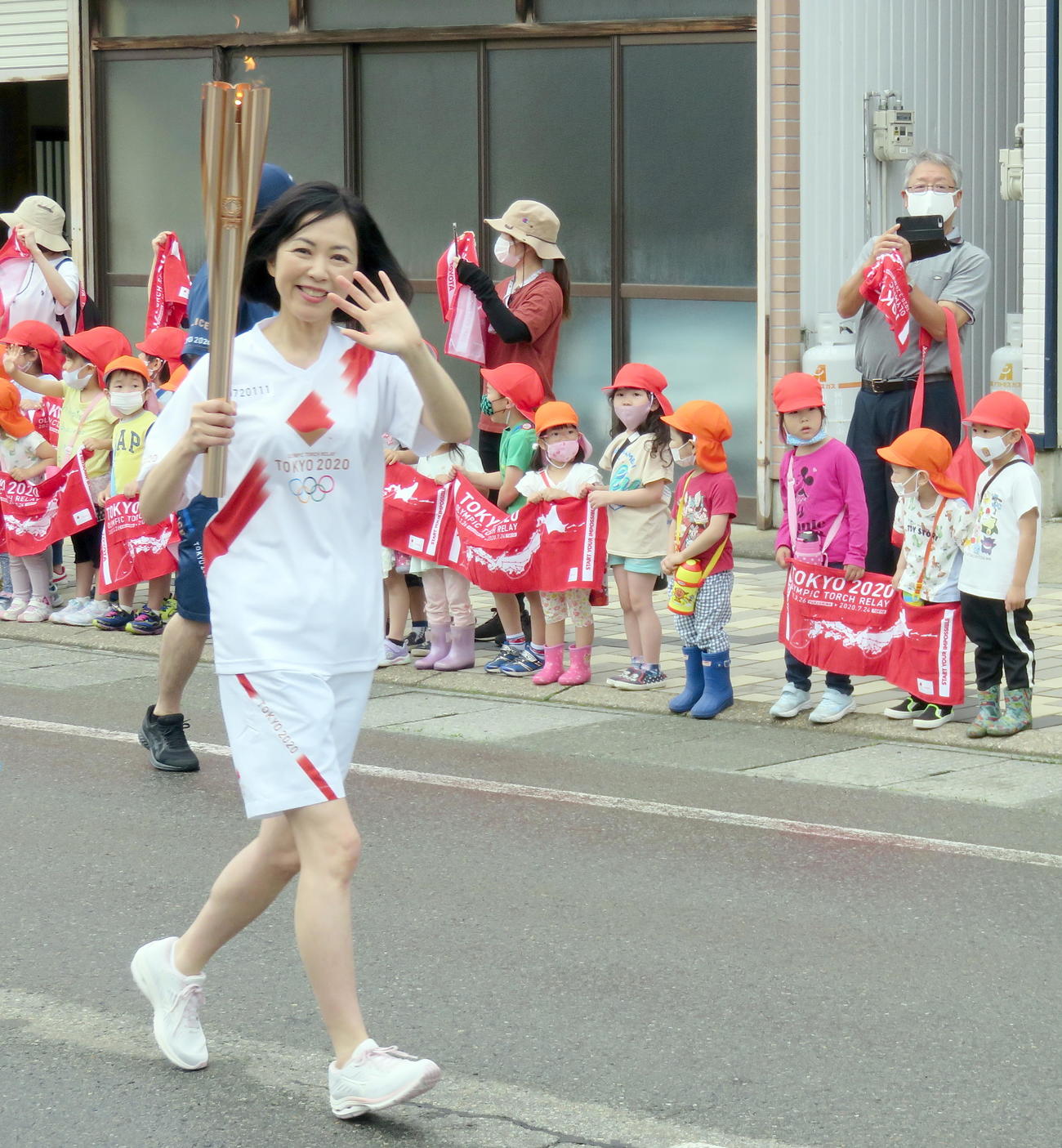 園児らの応援を背に笑顔で聖火ランナーを務めた小川選子さん（撮影・鎌田直秀）
