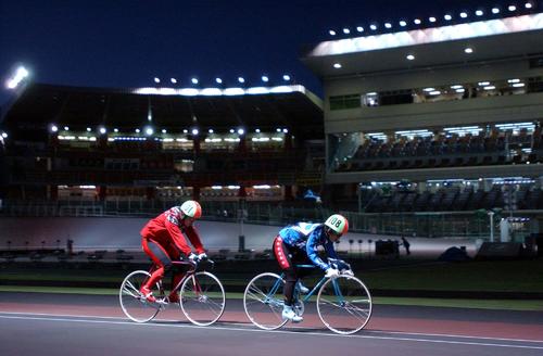 ナイター照明の中、夕方の指定練習で自転車を乗り込む松本整（左）と村上義弘（2002年12月29日撮影）
