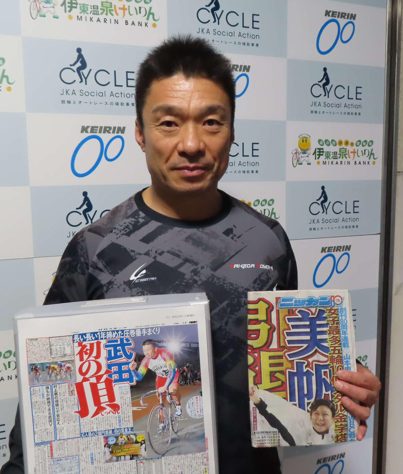 武田豊樹が自身のGP制覇を報じる14年12月31日付コピー（左）と5日付紙面を手にメッセージを寄せた