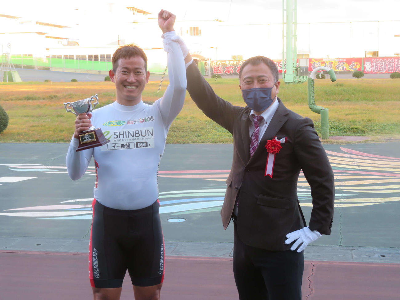 市田佳寿浩氏（右）から手渡された優勝カップを手に、笑顔でファンの声援に応える脇本雄太（左）