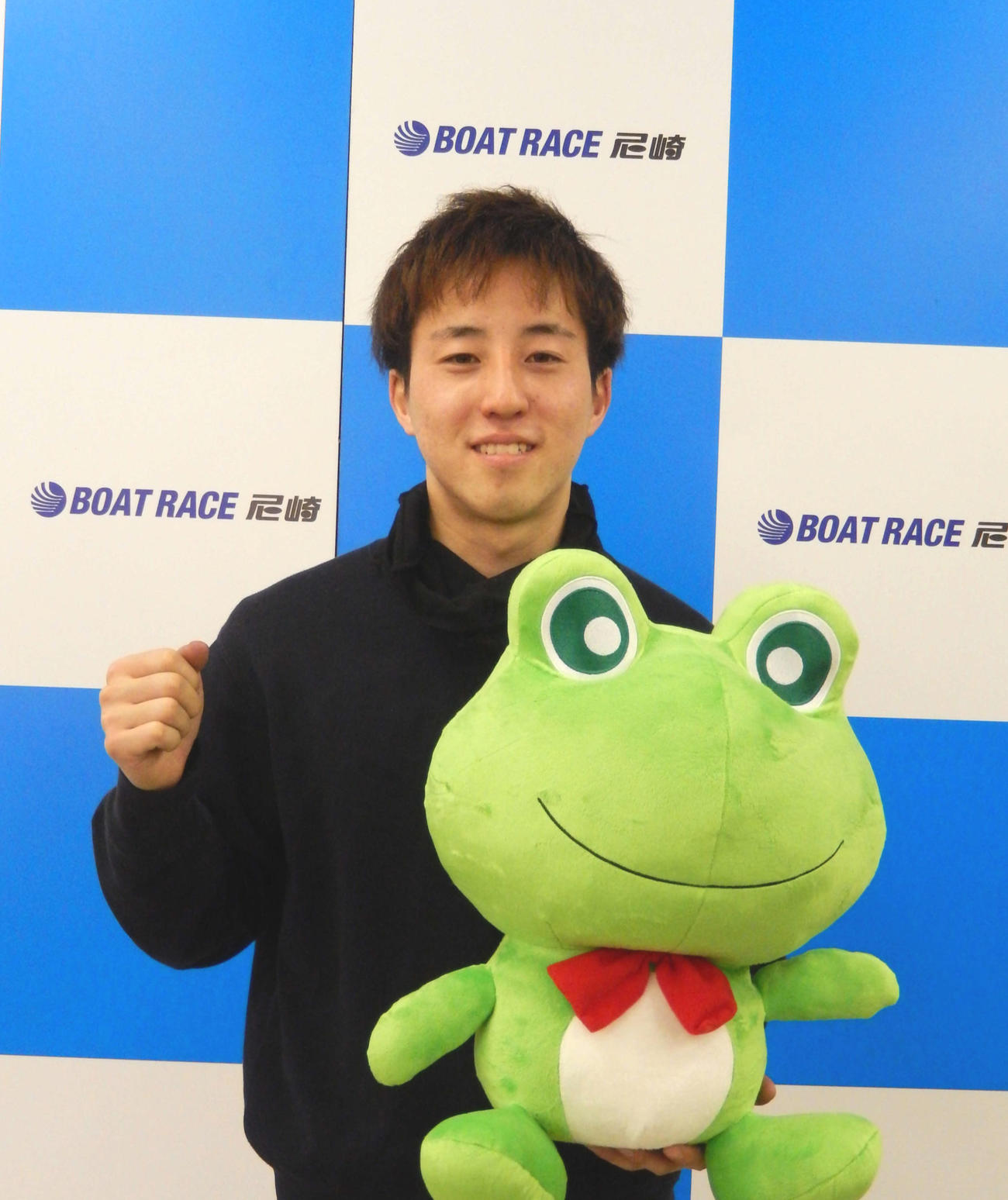 デビュー初勝利を飾った大森翼が、尼崎ボートのマスコット・センプル君のぬいぐるみを手に、笑顔でガッツポーズ