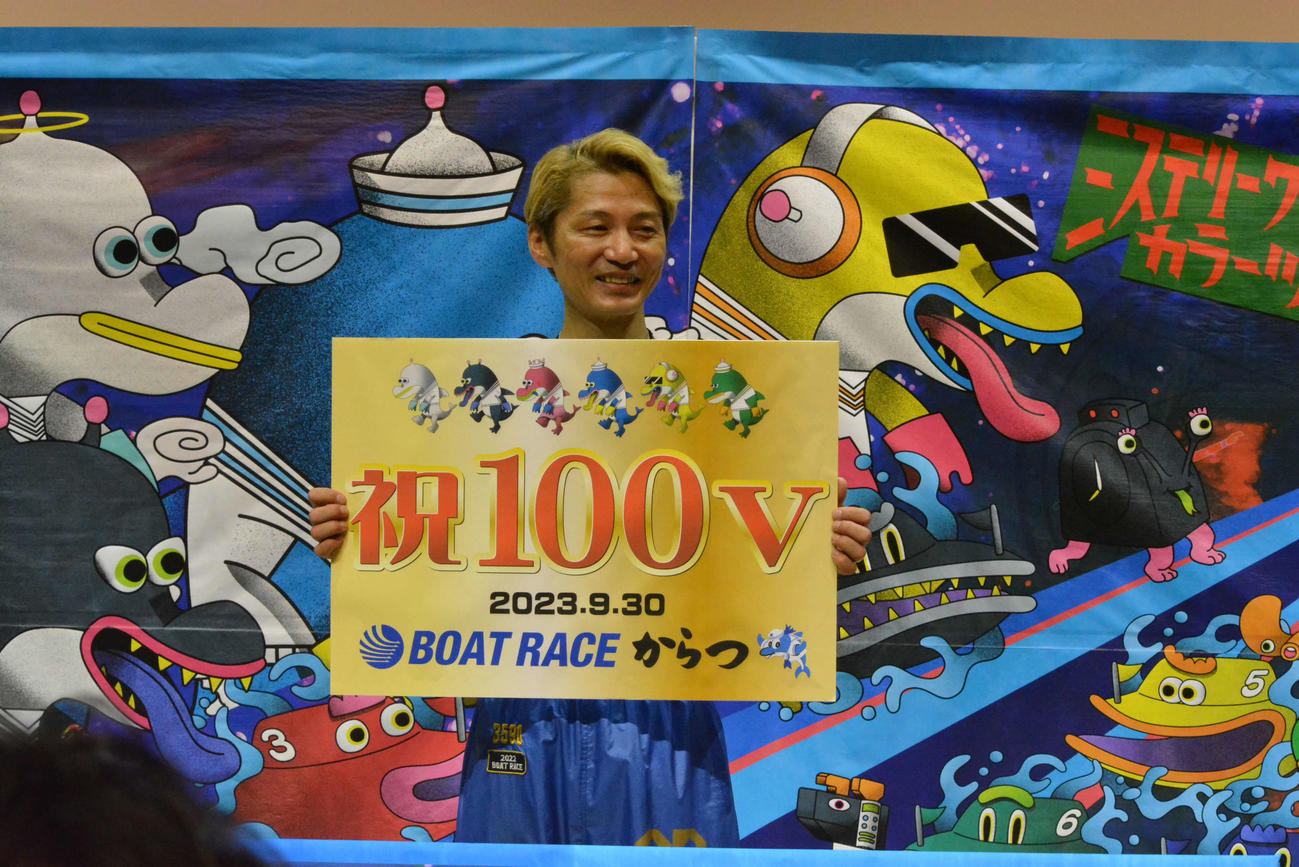 祝100Vのボードを手に笑顔の浜野谷憲吾