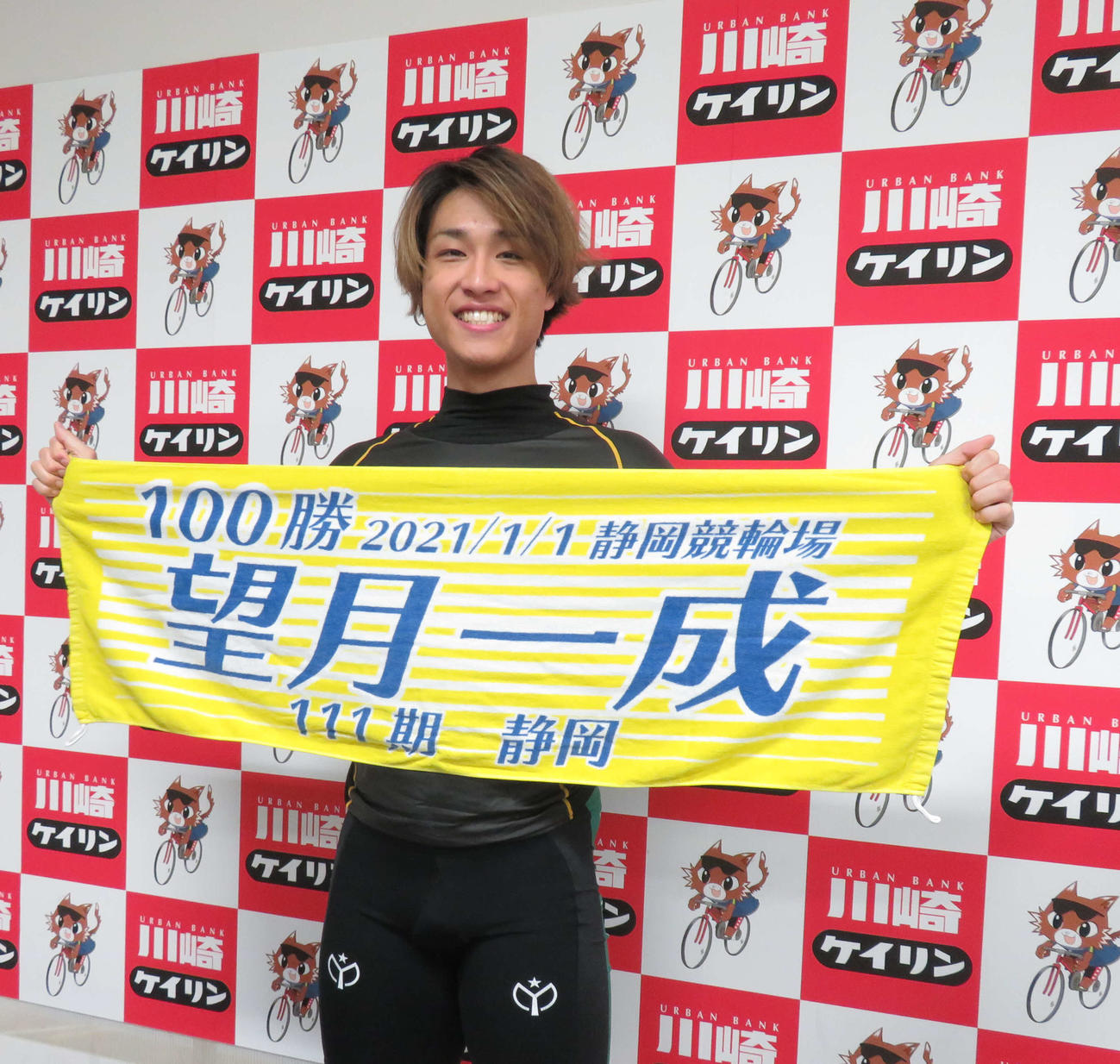 同期・望月一成の100勝記念タオルを掲げて自身の通算100勝の喜びを表す布居大地（撮影・栗田文人）