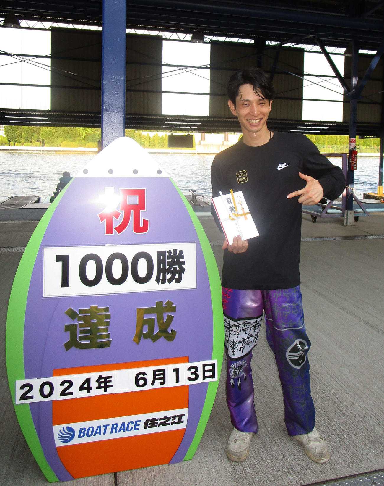 通算1000勝を達成し、記念ボードの前で笑顔を見せる高野哲史（撮影・安井雅彦）
