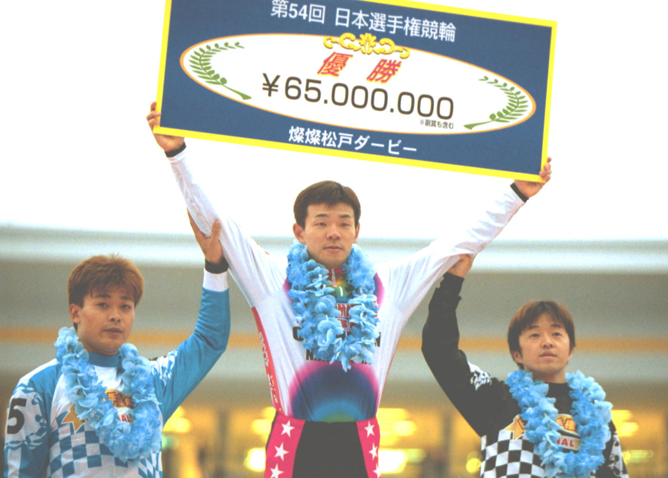 松戸競輪場で行われた日本選手権で優勝し、表彰台で賞金ボードを掲げる稲村成浩（中央）と、決勝2着の児玉広志（右）、3着の一丸安貴（2001年3月25日撮影）