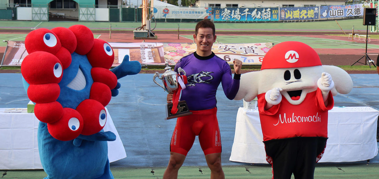 優勝した脇本雄太（中央）はミャクミャク（左）とムコリンムッチーにはさまれて笑顔