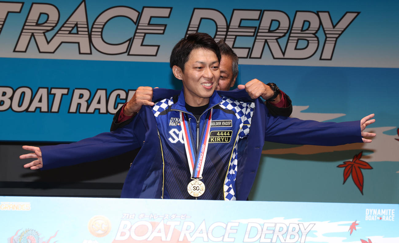 日本モーターボート競走会戸田支部の小林雅人執行役員からジャケット着せてもらう桐生順平（撮影・柴田隆二）
