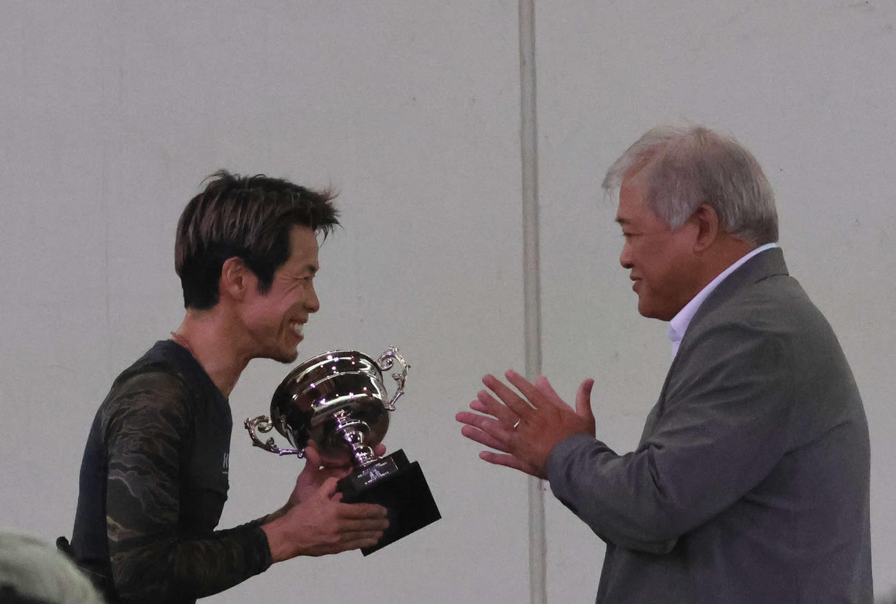 優勝した杉山正樹が本社の津波謙次メディア事業部公営戦略部長（写真右）から優勝カップが手渡され、笑顔を浮かべた