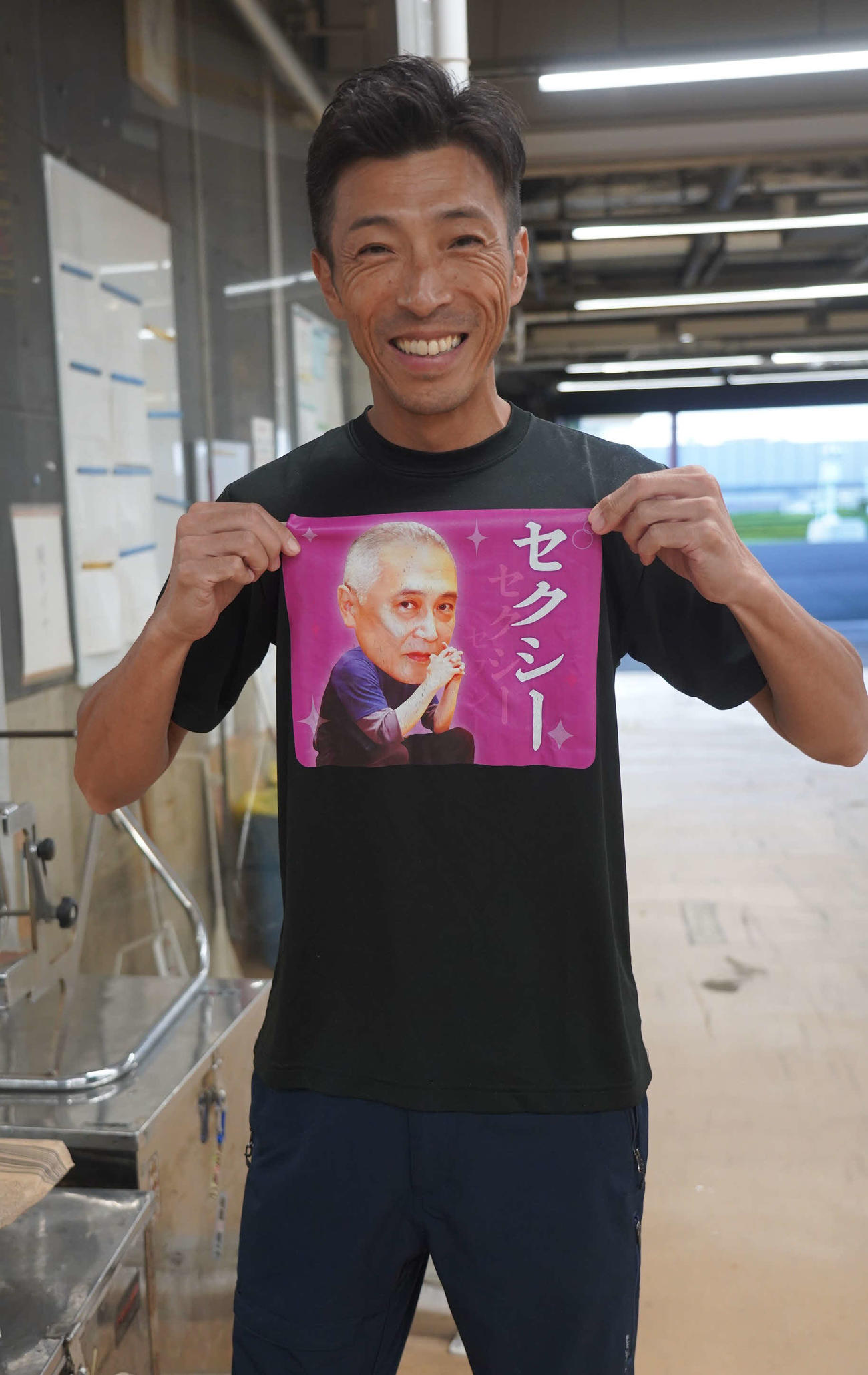 青木治親が梅内幹雄がモデルのTシャツを掲げて笑顔