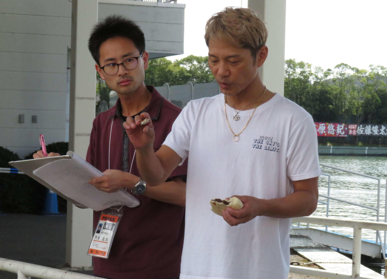 コイに餌を与えながら取材を受ける浜野谷憲吾