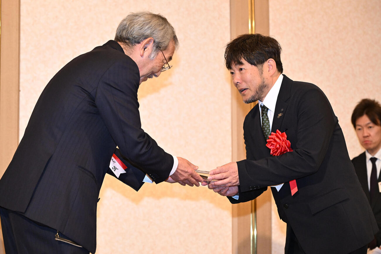 日刊スポーツ制定2025年第39回競輪年間三賞表彰式　ガールズ特別賞を受賞した佐藤水菜の代理で日刊スポーツの高田社長（左）からトロフィーを受け取る日本競輪選手会の古原常務理事（撮影・千葉一成）