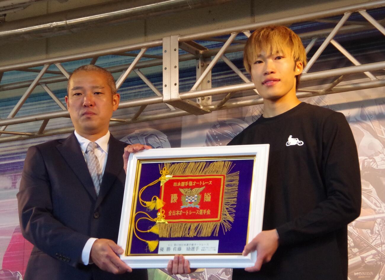 日本選手権優勝旗返還セレモニーで優勝旗レプリカを受け取った佐藤励。左は浜松支部選手会役員の柴田紘志