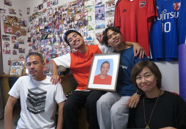 コウの遺影を囲み、笑顔を見せる両親とサッカー部同期の仲間