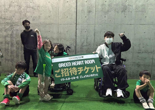 「グリーン・ハート・ルーム」への招待パネルを受け取り笑顔を見せる