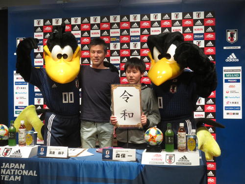 日本代表の公式記者会見場での撮影イベントで、日本代表マスコットのカララ(左)とカラッペ(右)とともに「令和」のボードを掲げて記念撮影するファン