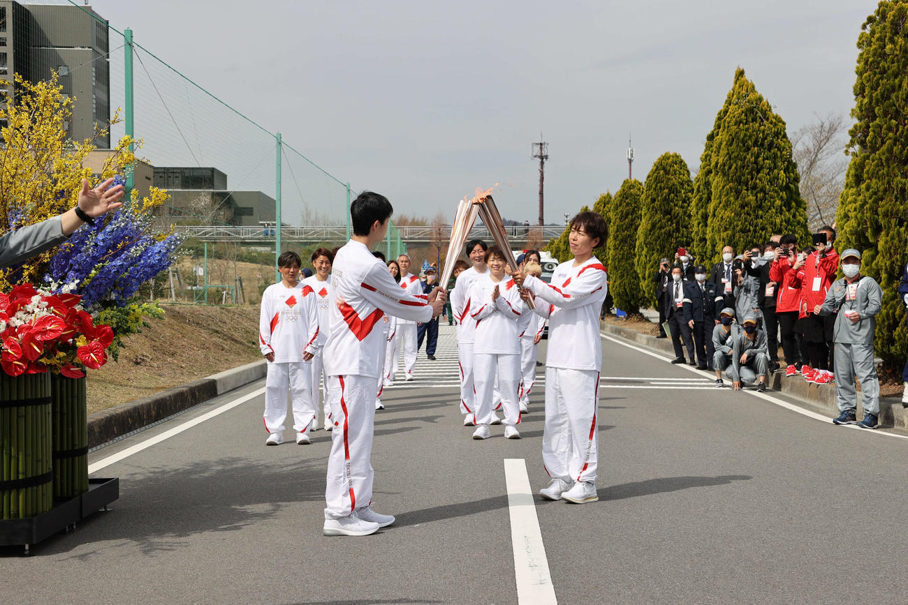 東京五輪の聖火リレーがスタートし、第2走者の大和田朝斗さん（左手前）にトーチキスで聖火をつなぐ、第1走者の、2011年サッカー女子W杯で優勝した日本代表「なでしこジャパン」岩清水梓（代表撮影）