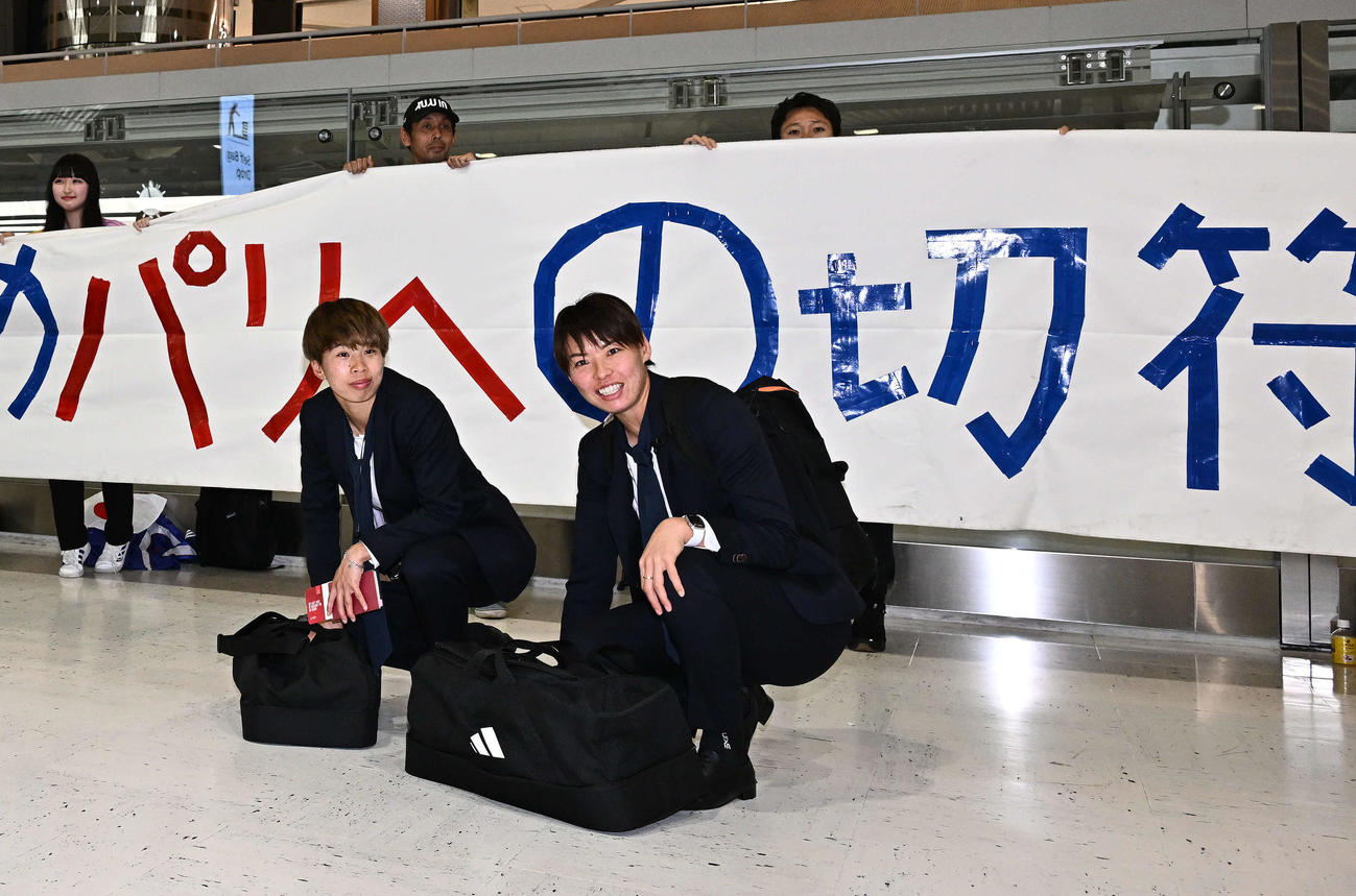 成田空港からサウジアラビアのジッダへ出発するなでしこジャパンの田中美（左）と熊谷はサポーターの横断幕を背に記念撮影する（撮影・滝沢徹郎）