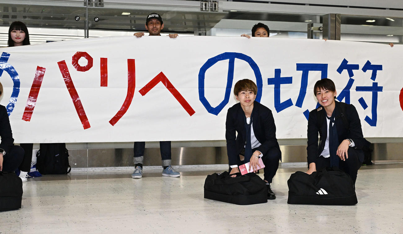 成田空港からサウジアラビアのジッダへ出発する、なでしこジャパンの田中美（左）と熊谷はサポーターの横断幕を背に記念撮影する（撮影・滝沢徹郎）