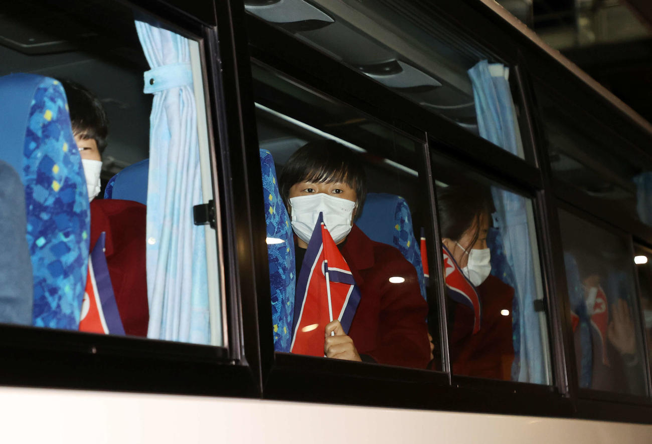 2月25日、来日し国旗を手にバスに乗るサッカー女子北朝鮮代表の選手たち（撮影・鈴木正人）