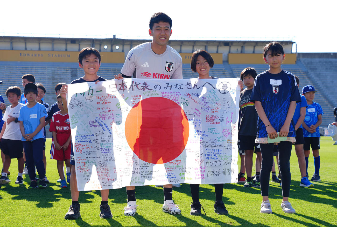 練習前に子どもたちから寄せ書き入りの日の丸を送られ記念写真に納まる遠藤（中央左）（撮影・垰建太）