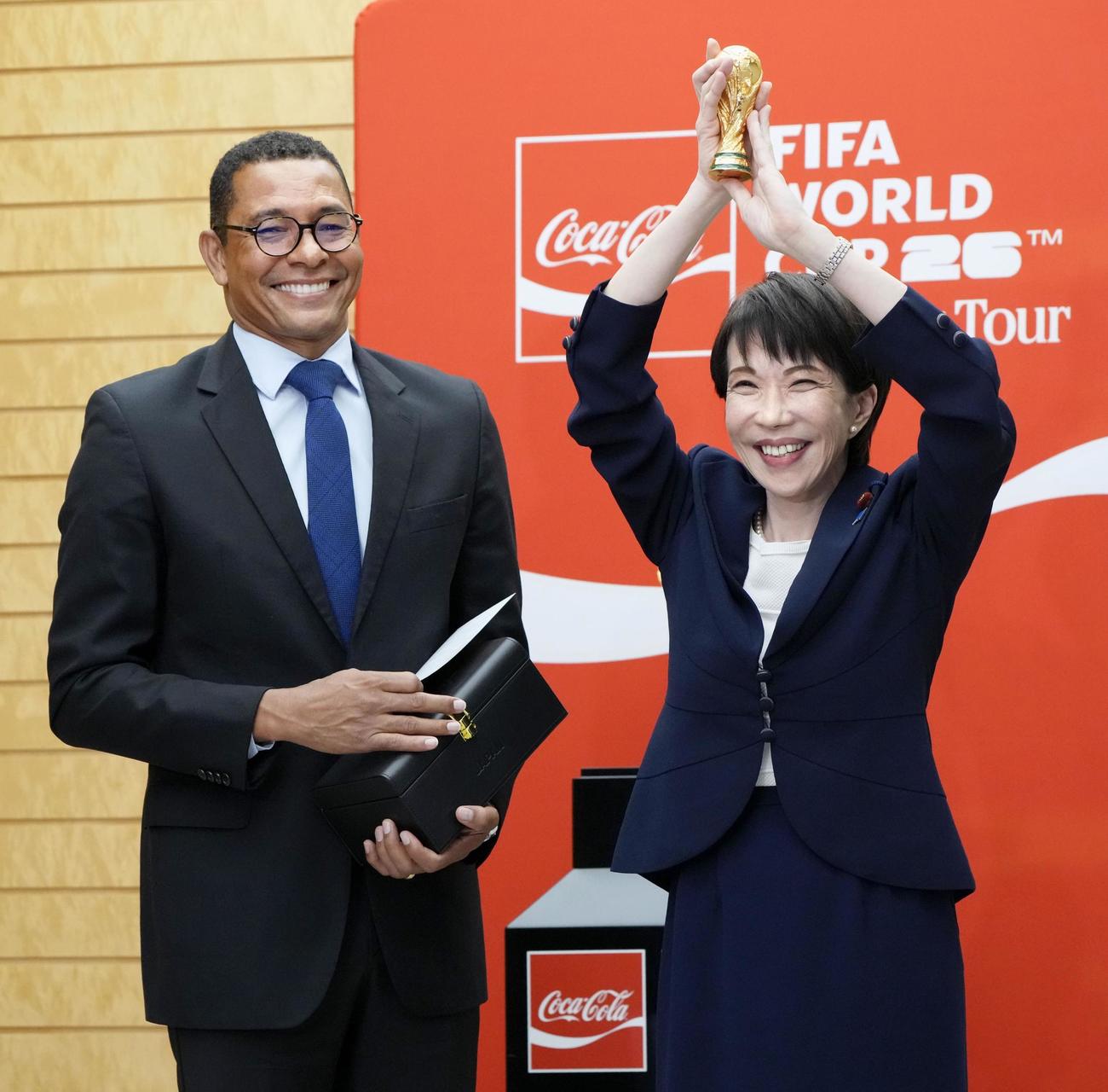 ジウベルトシウバ氏（左）からプレゼントされた、サッカーW杯のミニチュアトロフィーを掲げる高市首相（共同）