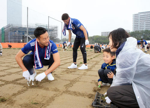 JFA夢フィールドでのポット苗植え付けイベントで、一般参加の子どもと苗を植える吉田（左）。奥は酒井（撮影・浅見桂子）