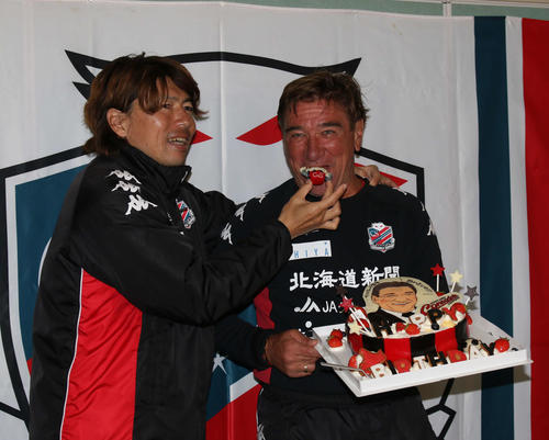 61歳の誕生日を迎え、ドーレくんのデコレーションを杉浦コーチ兼通訳（左）に口に運んでもらう札幌ペトロビッチ監督（2018年10月18日）