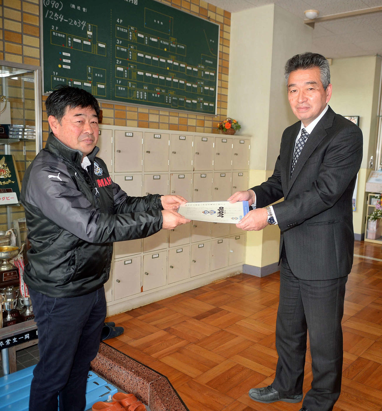 磐田ホームタウン部の大石氏（左）が磐田東部小の青島校長に祝電を手渡す