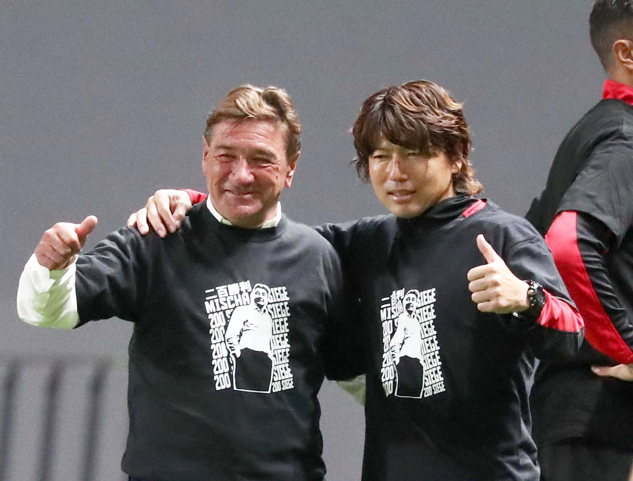 試合後、200勝記念Tシャツを着て記念撮影する杉浦コーチ兼通訳（右）とペトロビッチ監督（撮影・黒川智章）